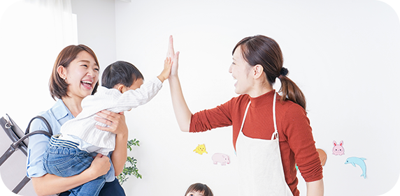 抱きかかえられている子供とハイタッチする保育士